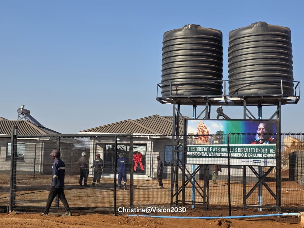Completed Presidential War Veteran Borehole installation in rural Zimbabwe with twin water tanks and Mnangagwa programme signage